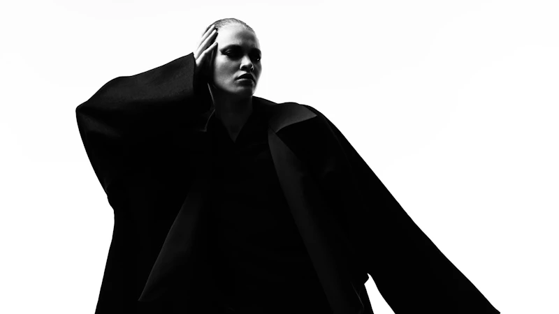 A person in a wide-sleeved black jacket posing in silhouette against a white background