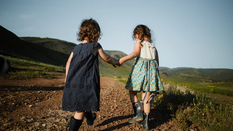 2 girls in blue dress standing on brown field during daytime