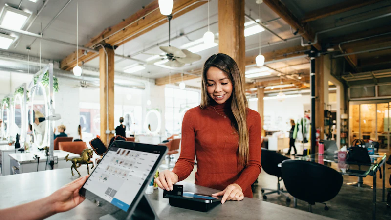 A woman in a rust-colored sweater paying with a card at a salon counter