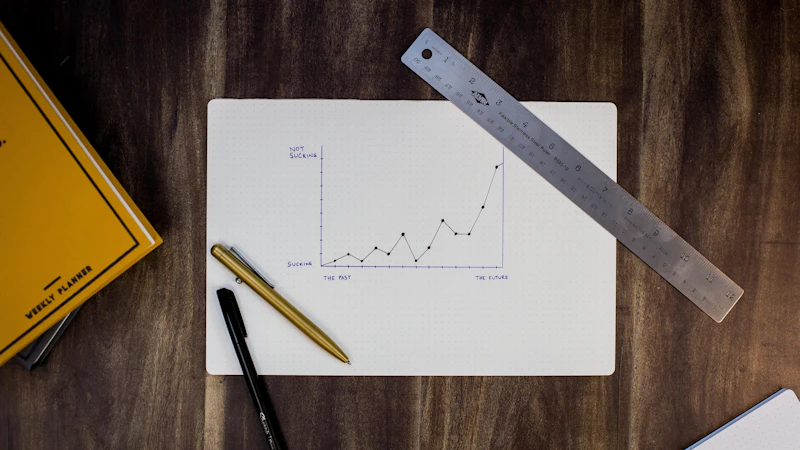 A hand-drawn line graph on paper with a metal ruler and two pens