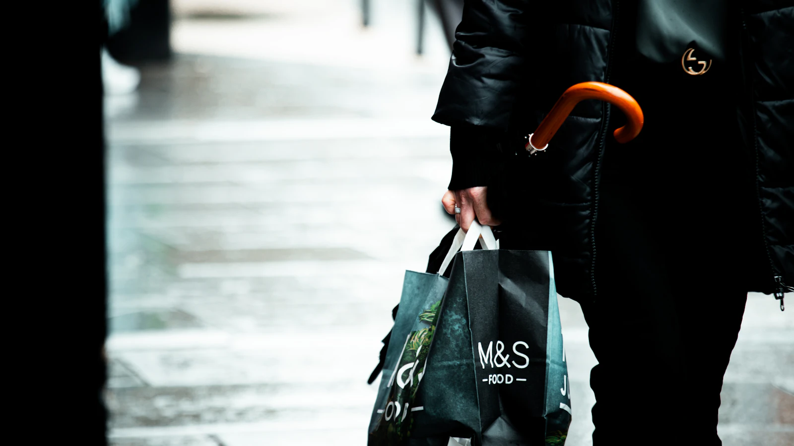 Person holding shopping bag and umbrella on wet street