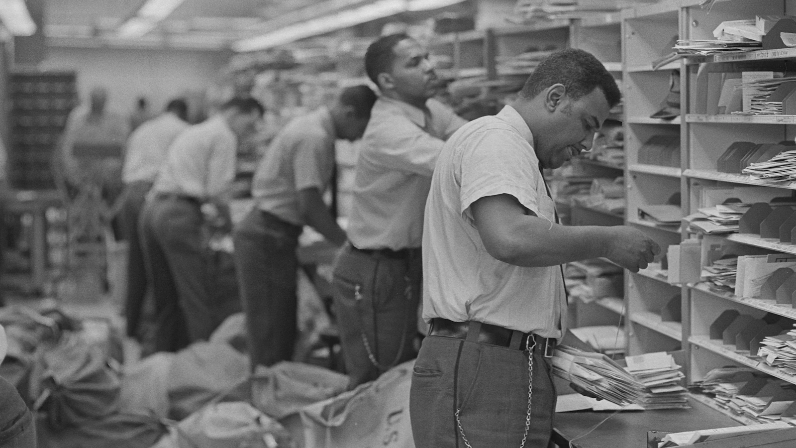 African American postal employees sorting mail into cubby-holes