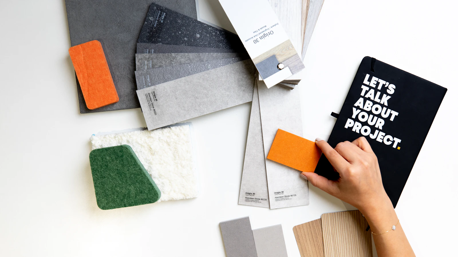 A person holding an orange material sample over a white desk with design swatches
