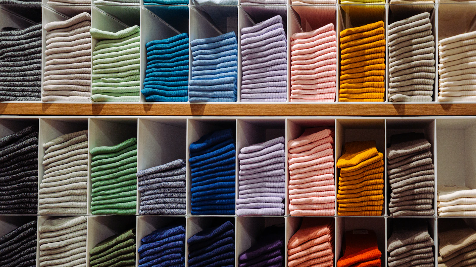 Stacks of folded colorful socks organized by color on wooden retail store shelves